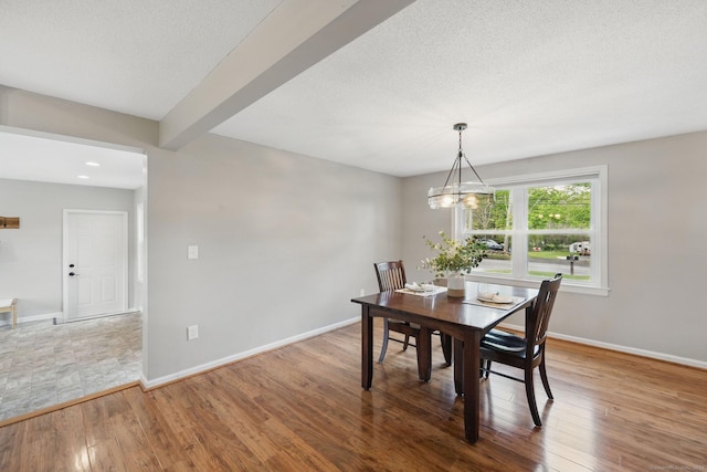 dining area featuring wood finished floors, baseboards, a chandelier, a textured ceiling, and beamed ceiling