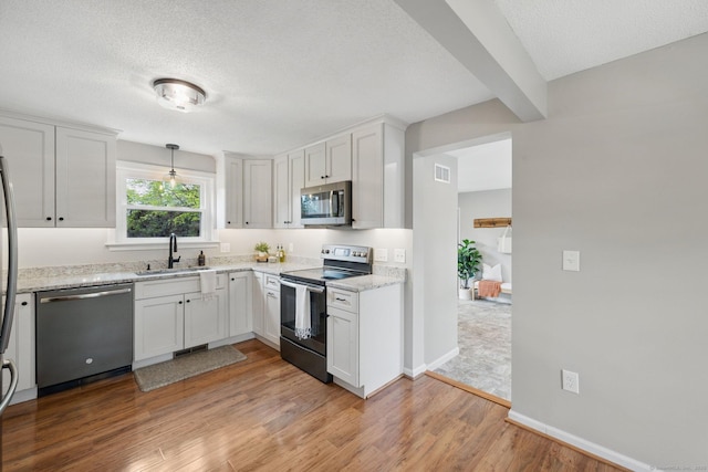 kitchen with stainless steel appliances, a sink, light wood-style floors, baseboards, and white cabinets