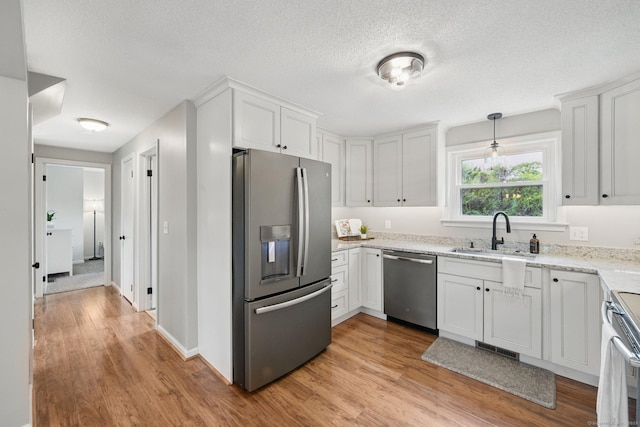 kitchen with stainless steel appliances, a sink, light wood-style floors, white cabinets, and light stone counters
