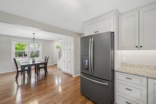 kitchen with stainless steel fridge with ice dispenser, white cabinetry, light wood-style flooring, baseboards, and light stone counters