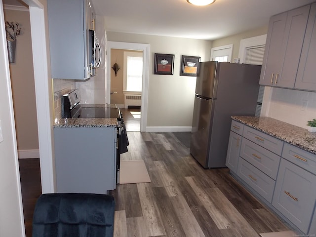 kitchen with backsplash, radiator, dark wood finished floors, light stone counters, and stainless steel appliances