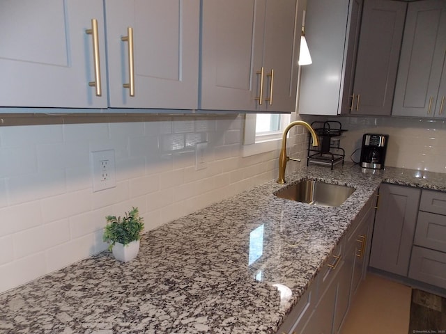 kitchen with light stone counters, gray cabinets, tasteful backsplash, and a sink