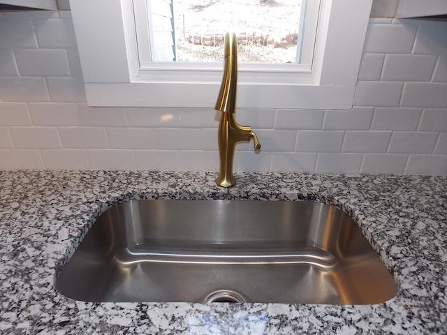 room details featuring a sink, light stone countertops, and backsplash