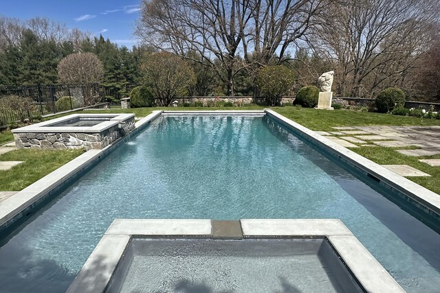 view of pool with a pool with connected hot tub, fence, and a lawn