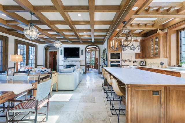 kitchen featuring a notable chandelier, stone tile floors, coffered ceiling, open floor plan, and arched walkways