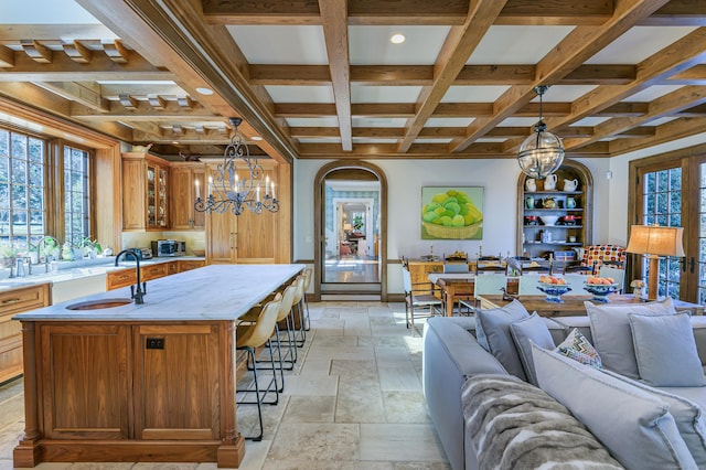 kitchen featuring a sink, an inviting chandelier, stone tile floors, open floor plan, and coffered ceiling