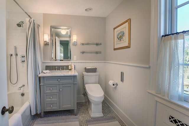 full bath with toilet, vanity, shower / bath combo with shower curtain, and a wainscoted wall