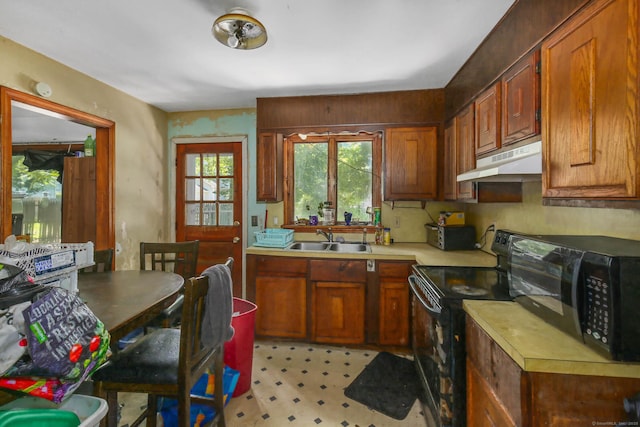 kitchen with black appliances, under cabinet range hood, a sink, light countertops, and light floors