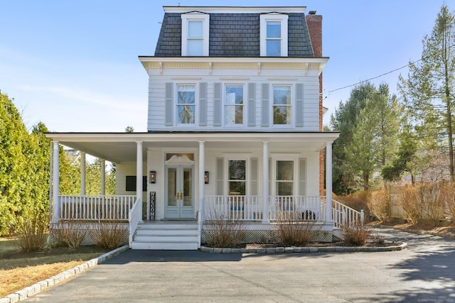 victorian home featuring covered porch, french doors, a chimney, and mansard roof