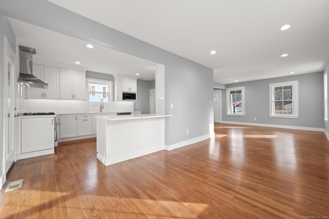 kitchen with tasteful backsplash, wall chimney range hood, visible vents, light countertops, and built in microwave