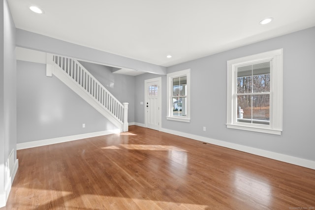 unfurnished living room with wood finished floors, recessed lighting, baseboards, and stairway