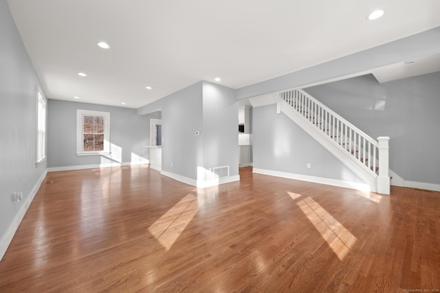 unfurnished living room with wood finished floors, baseboards, visible vents, and stairs