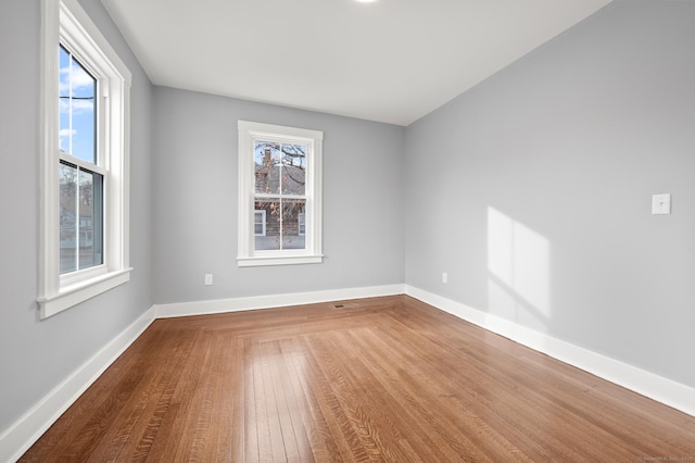 spare room with baseboards, wood finished floors, and a healthy amount of sunlight