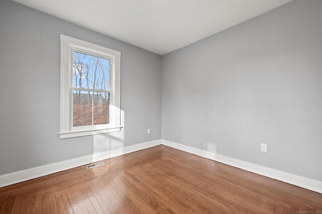 empty room with hardwood / wood-style floors, baseboards, and visible vents