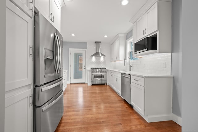 kitchen with tasteful backsplash, appliances with stainless steel finishes, wall chimney range hood, and light wood-style floors