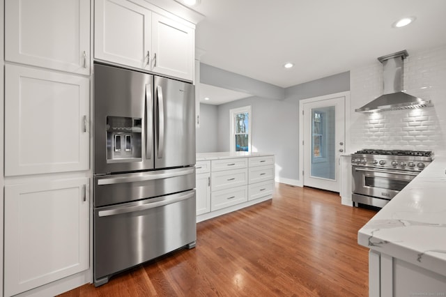 kitchen with wall chimney exhaust hood, light stone countertops, white cabinetry, wood finished floors, and stainless steel appliances
