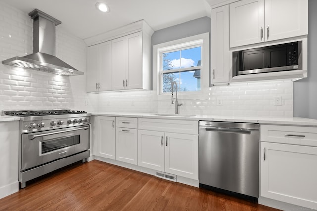 kitchen featuring appliances with stainless steel finishes, wall chimney range hood, visible vents, dark wood finished floors, and a sink