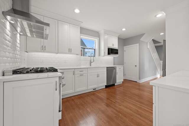 kitchen with light wood-style floors, stainless steel dishwasher, exhaust hood, white cabinetry, and backsplash