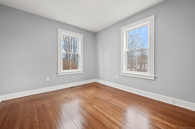 unfurnished room featuring visible vents, a wealth of natural light, wood finished floors, and baseboards