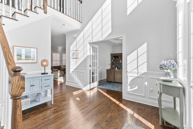 entryway featuring dark wood-type flooring, stairway, a decorative wall, and a wainscoted wall