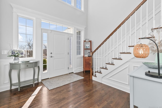 foyer with stairway, a wainscoted wall, a towering ceiling, wood finished floors, and a decorative wall