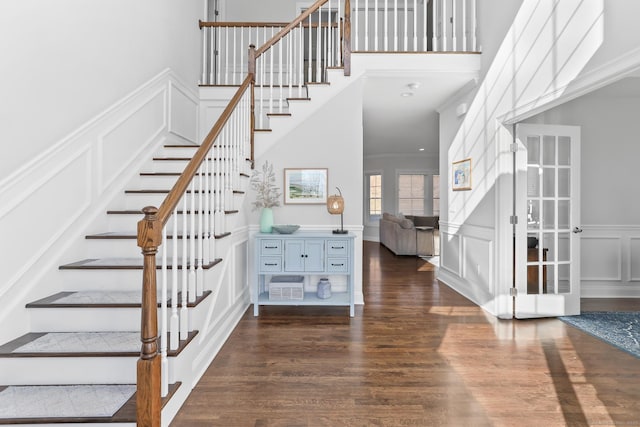 stairway with a wainscoted wall, wood finished floors, crown molding, and a decorative wall