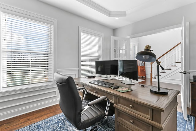 office featuring dark wood-type flooring, ornamental molding, wainscoting, a decorative wall, and a raised ceiling