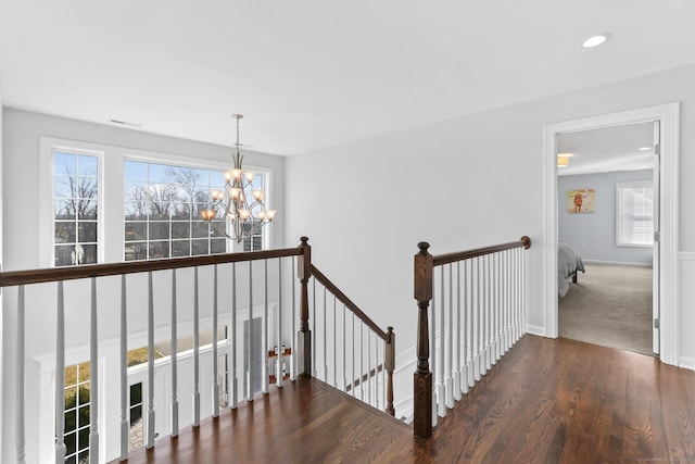 hall featuring a wealth of natural light, an upstairs landing, an inviting chandelier, and wood finished floors