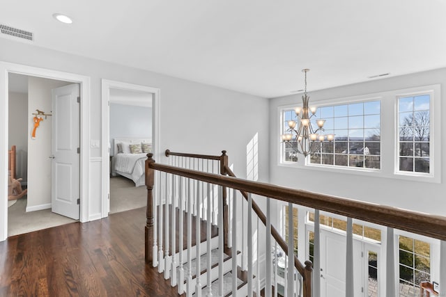 hallway featuring dark wood-type flooring, a notable chandelier, an upstairs landing, and visible vents