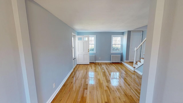 foyer with light wood-style flooring, radiator, baseboards, and stairway