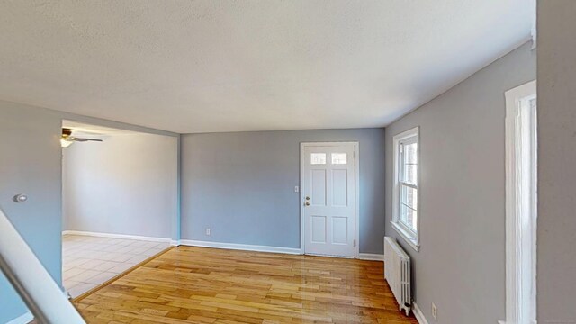 entrance foyer with light wood finished floors, radiator heating unit, a textured ceiling, baseboards, and ceiling fan