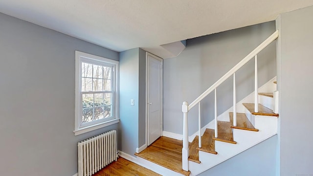 stairway with radiator, baseboards, and wood finished floors