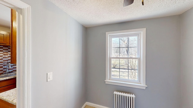 spare room featuring a sink, a ceiling fan, a textured ceiling, radiator, and baseboards