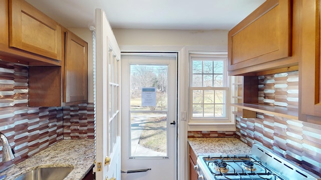 kitchen featuring a sink, brown cabinetry, backsplash, and range with gas stovetop