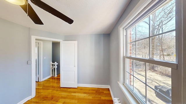 spare room with baseboards, a textured ceiling, a ceiling fan, and light wood finished floors
