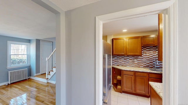 kitchen with light stone countertops, brown cabinets, a sink, radiator, and stainless steel refrigerator
