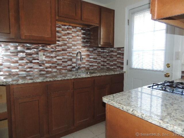 kitchen with a wealth of natural light, a sink, light stone countertops, and tasteful backsplash