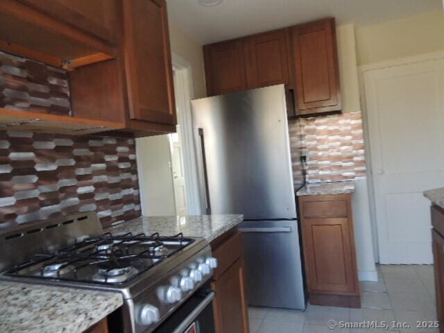 kitchen with light stone counters, tasteful backsplash, appliances with stainless steel finishes, brown cabinetry, and light tile patterned floors