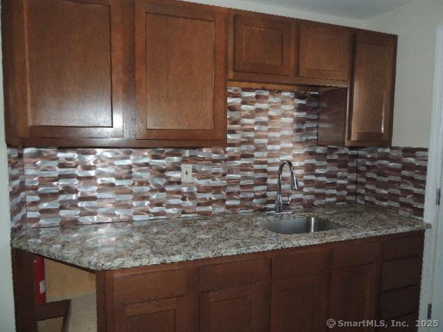 kitchen with brown cabinets, backsplash, light stone countertops, and a sink