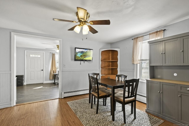 dining room featuring a baseboard heating unit, a wainscoted wall, wood finished floors, and a ceiling fan