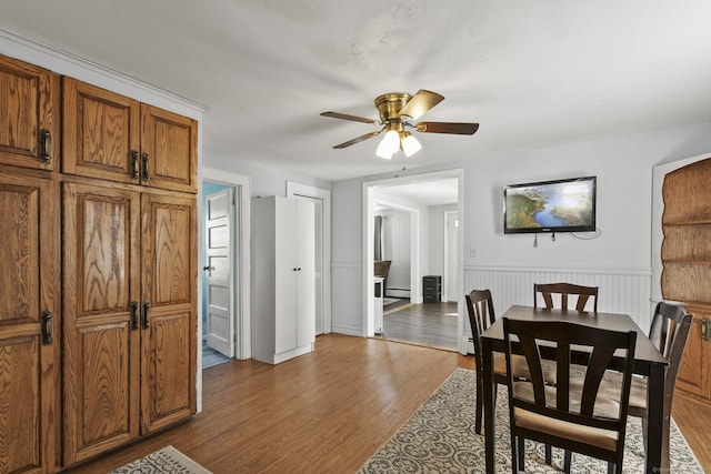 dining area with a baseboard radiator, a wainscoted wall, wood finished floors, and a ceiling fan