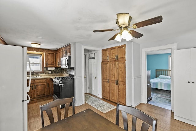 kitchen with a ceiling fan, wood finished floors, a sink, appliances with stainless steel finishes, and brown cabinets