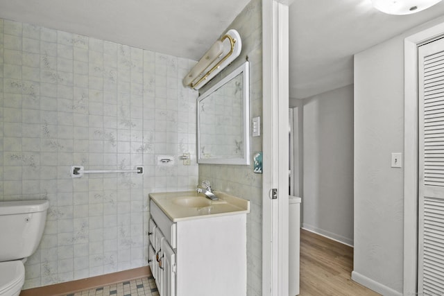 bathroom featuring baseboards, toilet, vanity, wood finished floors, and tile walls