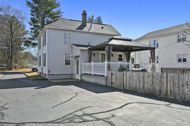 rear view of house with a gazebo, a shingled roof, a chimney, and fence