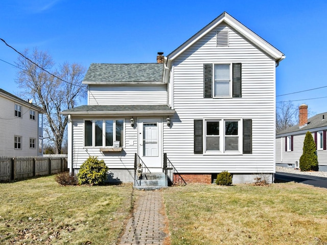 traditional home with entry steps, a shingled roof, a front yard, and fence