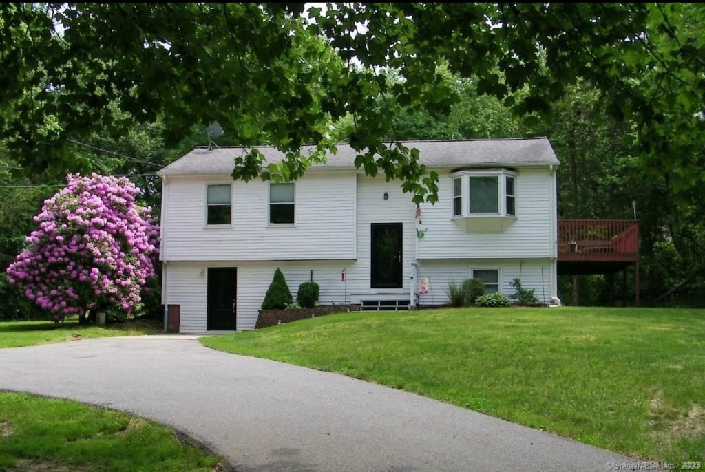 raised ranch with entry steps, a deck, driveway, and a front yard