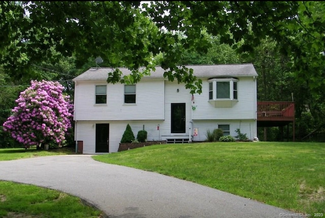 raised ranch with entry steps, a deck, driveway, and a front yard