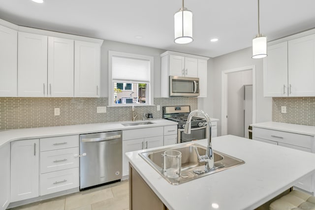 kitchen featuring an island with sink, hanging light fixtures, white cabinets, stainless steel appliances, and a sink