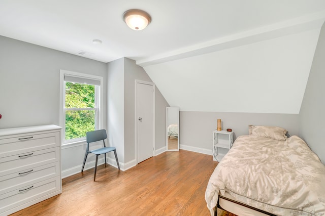 bedroom with light wood-style flooring, lofted ceiling, and baseboards