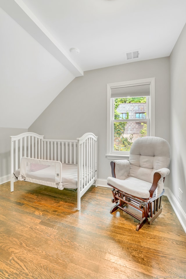 bedroom featuring visible vents, wood finished floors, a nursery area, baseboards, and vaulted ceiling with beams